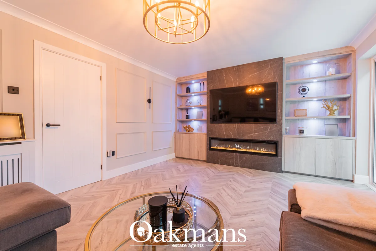 Luxury living room with marble fireplace, wall-mounted TV, illuminated shelving, herringbone flooring, gold ceiling fixt