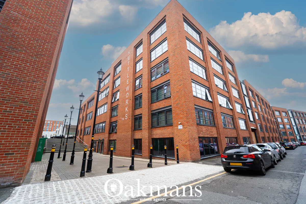 Modern brick apartment building with multiple storeys, corner position, large windows, street-level entrance, bollards a