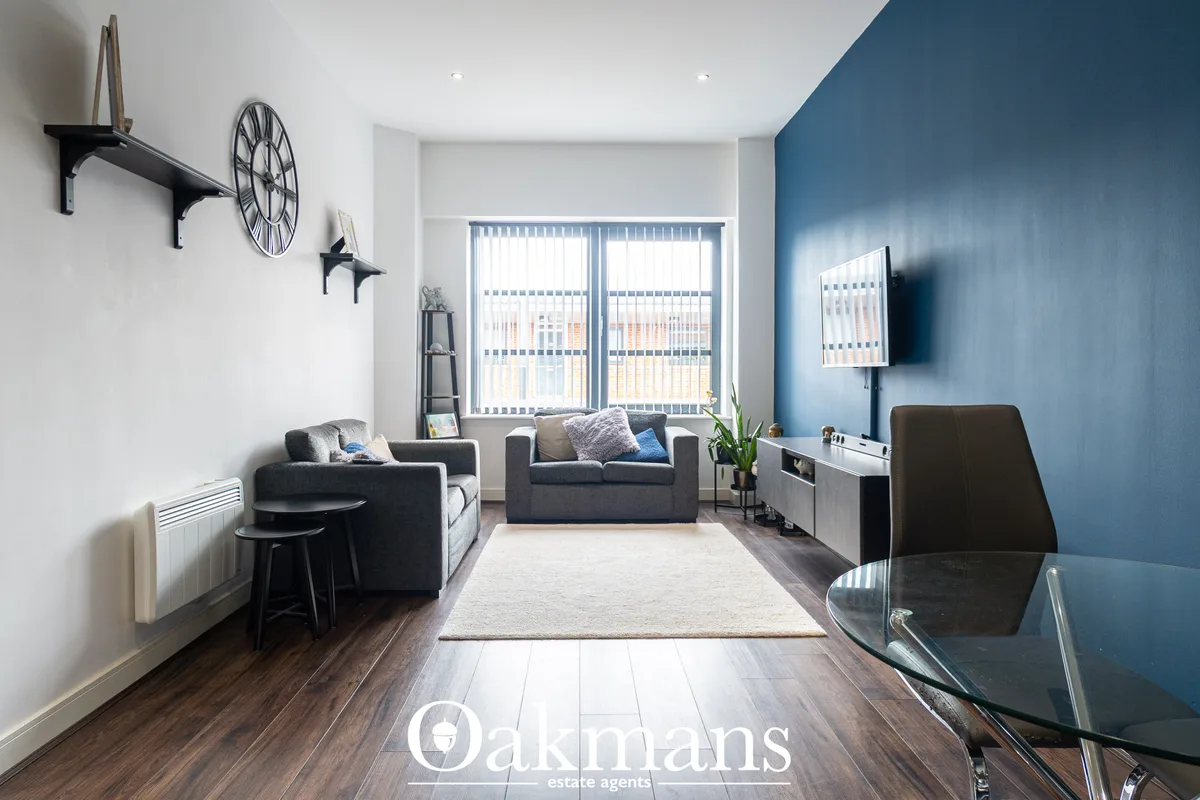 Modern living room with charcoal sofas, cream rug, blue accent wall, wall-mounted TV, clock and sculptural wall art, lar