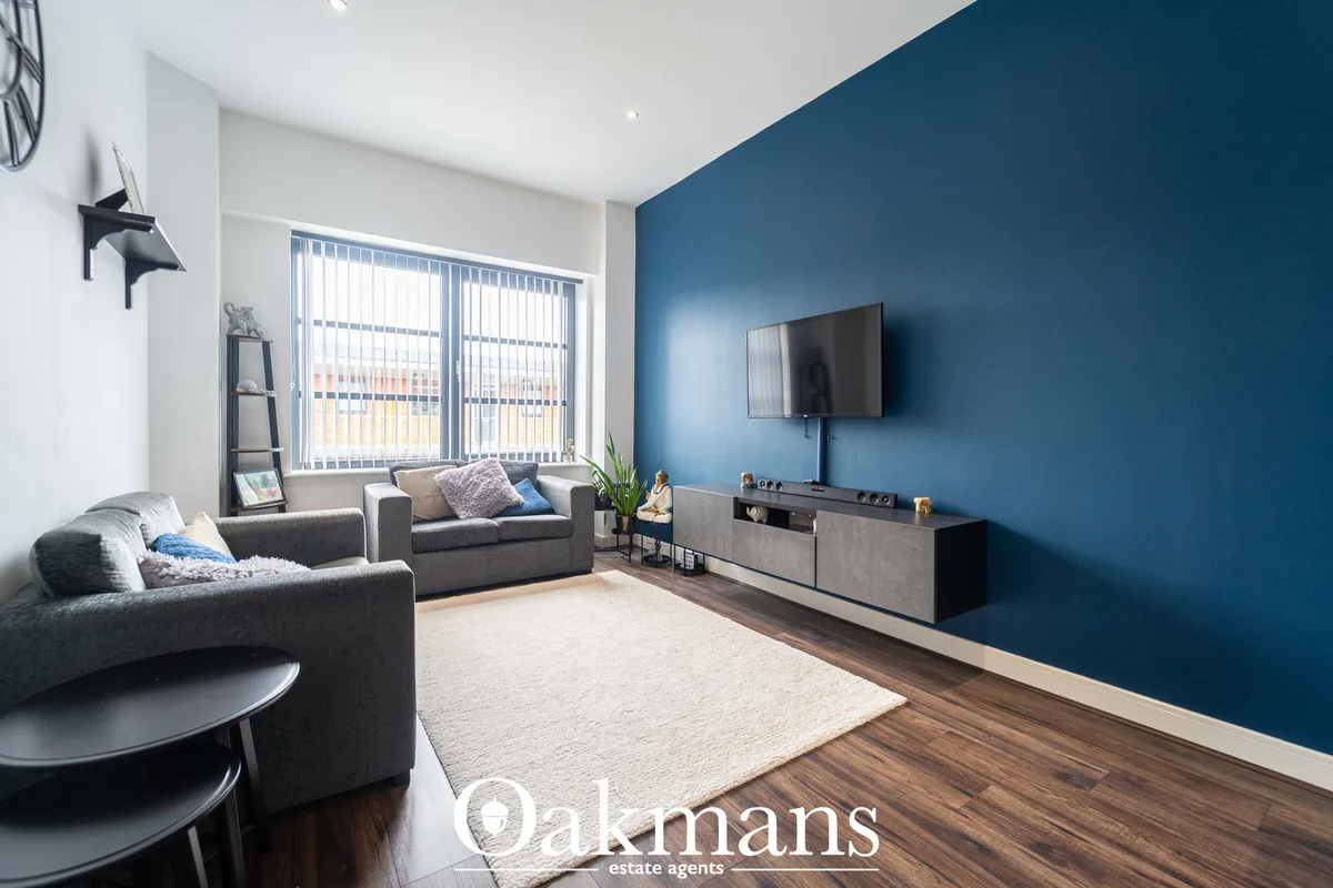 Modern living room with deep blue accent wall, grey corner sofa, wooden flooring, wall-mounted TV, cream rug and vertica