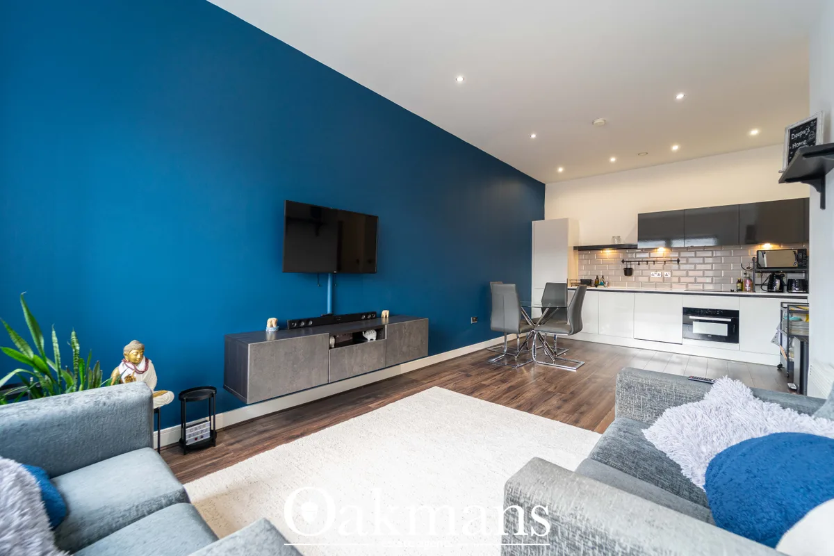 Open-plan living room with bold blue accent wall, modern grey sofa, wooden flooring, mounted flat-screen TV and adjacent
