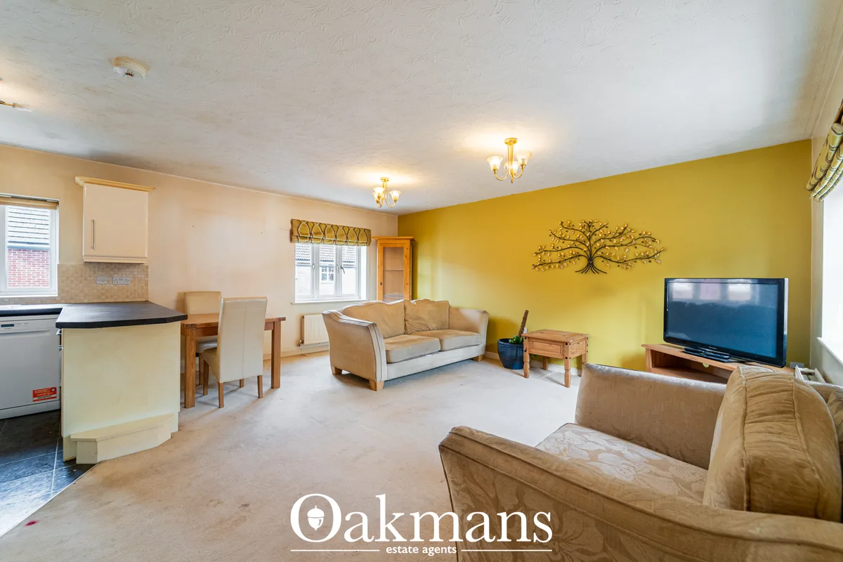 Spacious open-plan living area with yellow feature wall, beige sofas, flat-screen TV, wooden furniture and kitchen area 