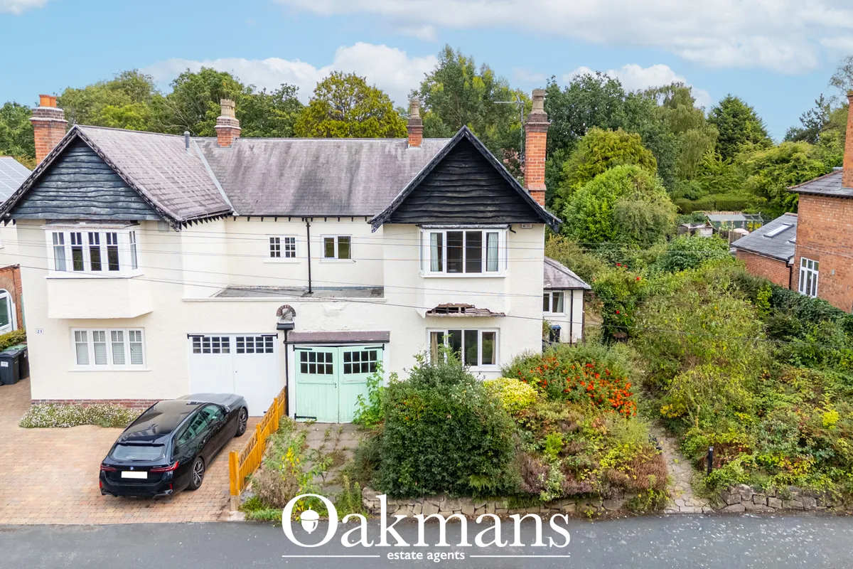 Two-storey cream and brick detached house with slate roof, bay windows, green garage doors, brick driveway with parked c