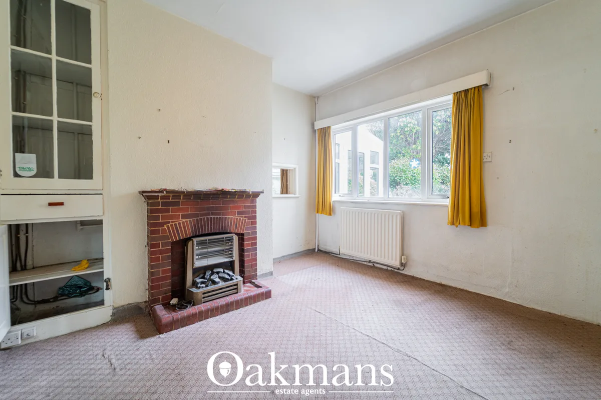 Spacious living room with red brick fireplace, electric fire, large bay window with yellow curtains, radiator, cream wal