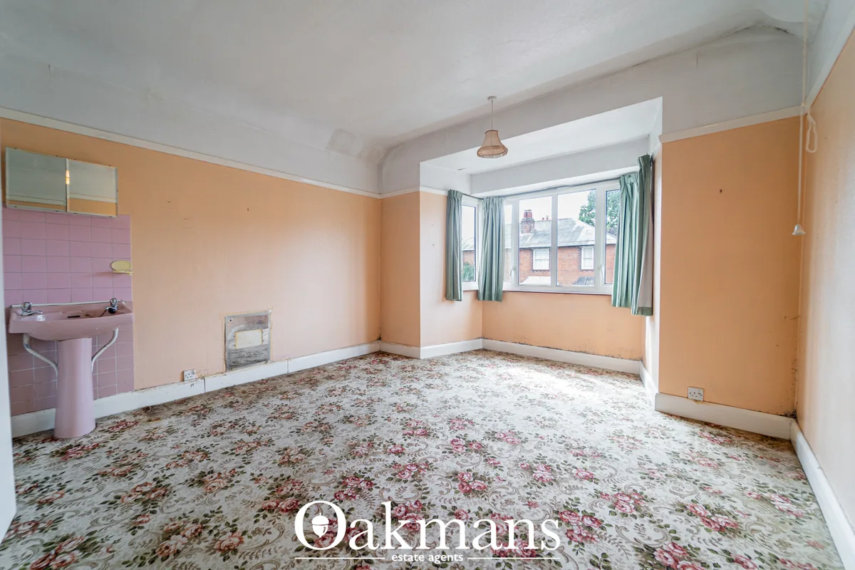 Spacious living room with peach-coloured walls, bay windows with green curtains, pink sink unit, patterned carpet and wh