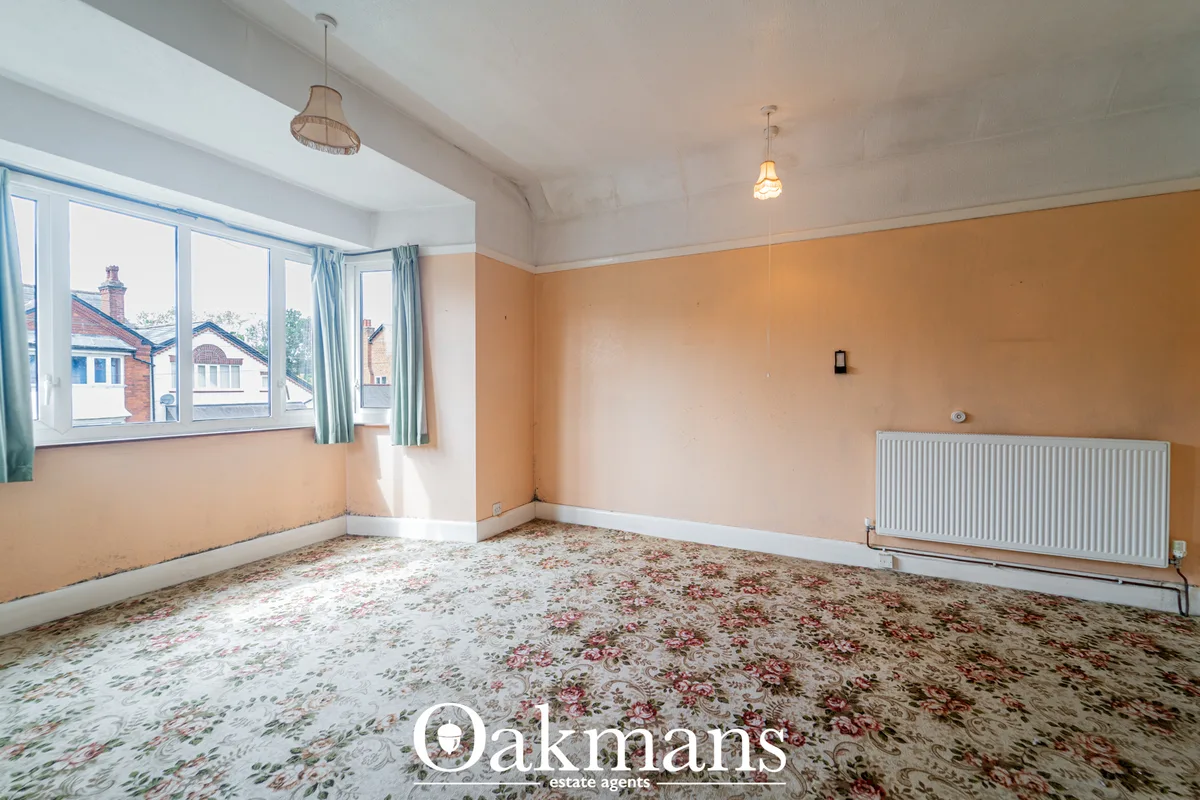 Spacious living room with peach-coloured walls, white ceiling, patterned carpet, radiator, pendant lighting and bay wind