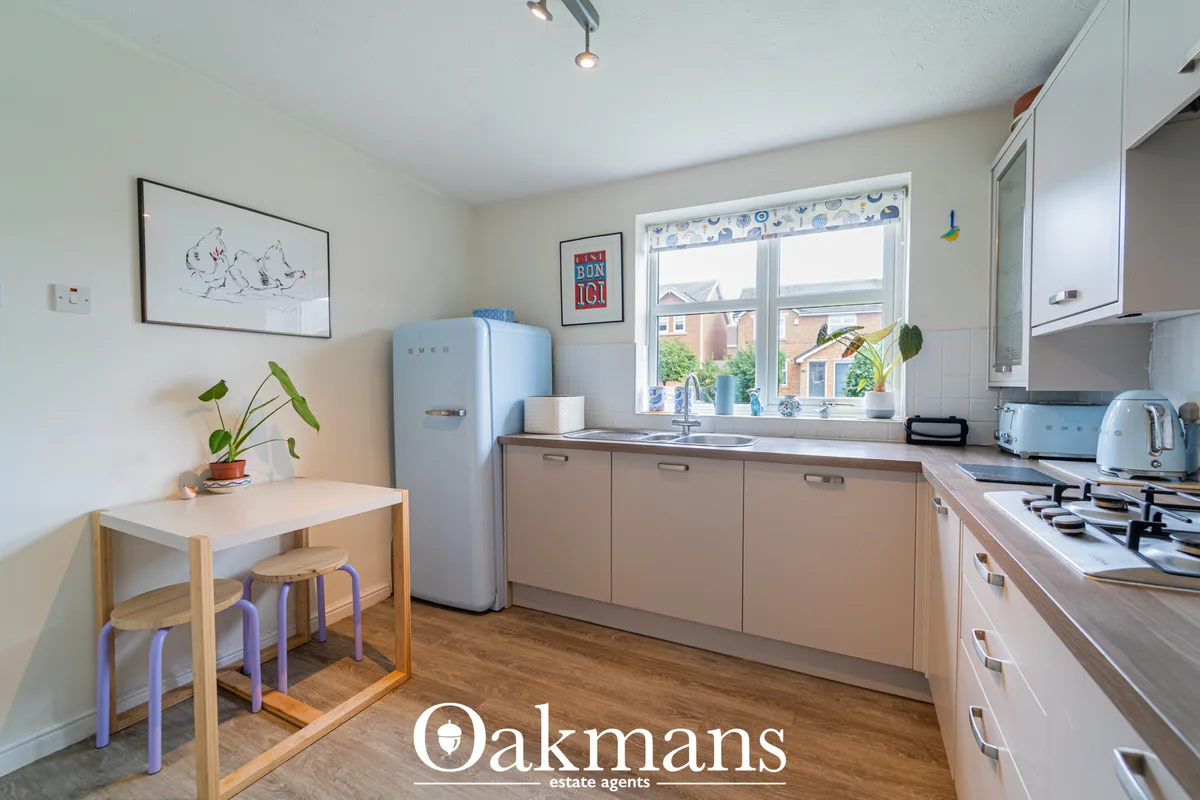 Modern kitchen with beige cabinetry, light blue retro fridge, gas hob, breakfast table with stools, and large window ove