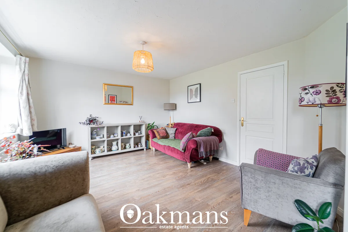 Spacious living room with cream walls, wooden flooring, pink sofa with cushions, grey armchair, storage shelving, pendan