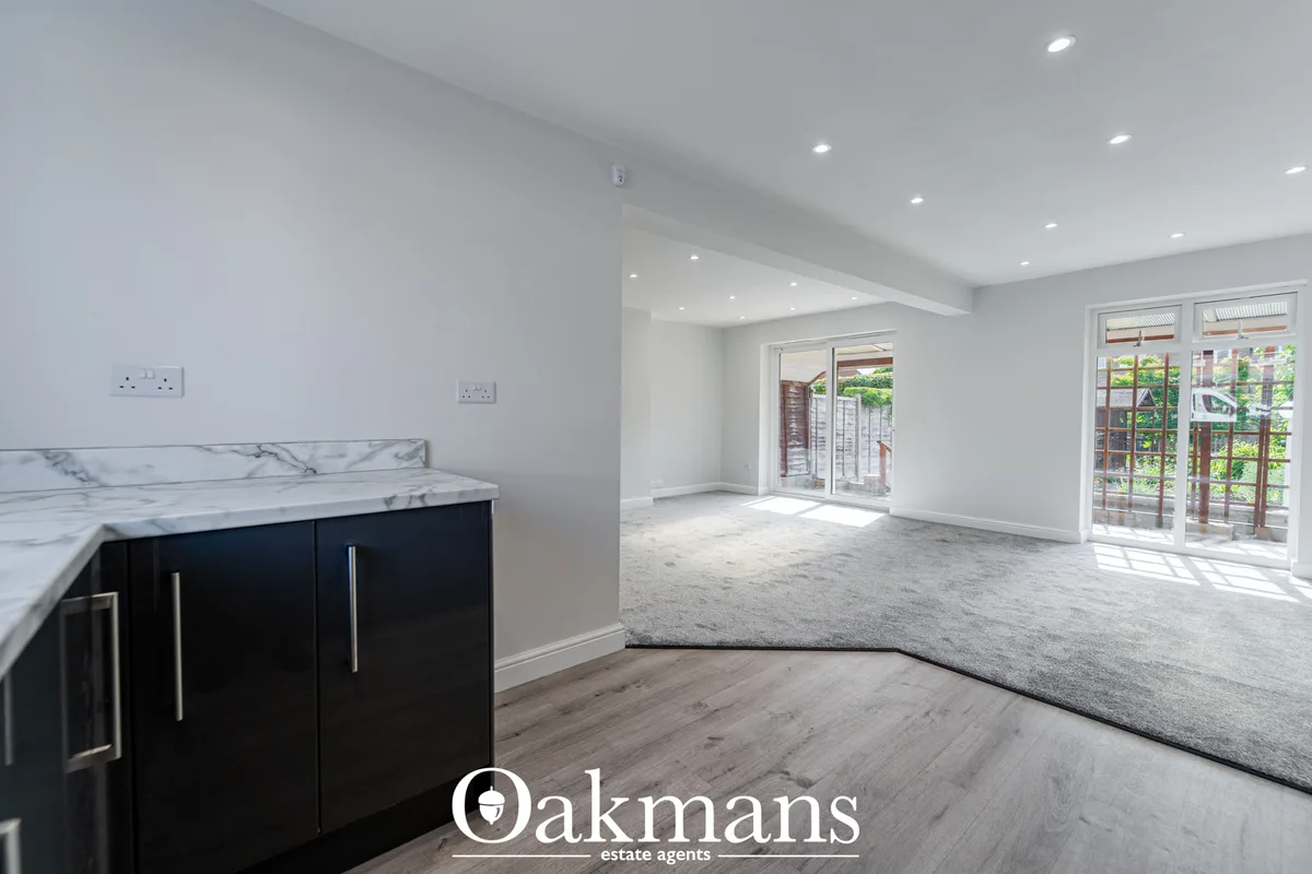 Bright open-plan living room with grey carpet, white walls, recessed ceiling lights, French doors to garden and fitted d