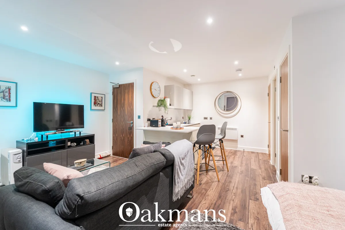Open-plan living room with grey sofa, flat-screen TV, integrated kitchen, breakfast bar with grey stools, wooden floorin