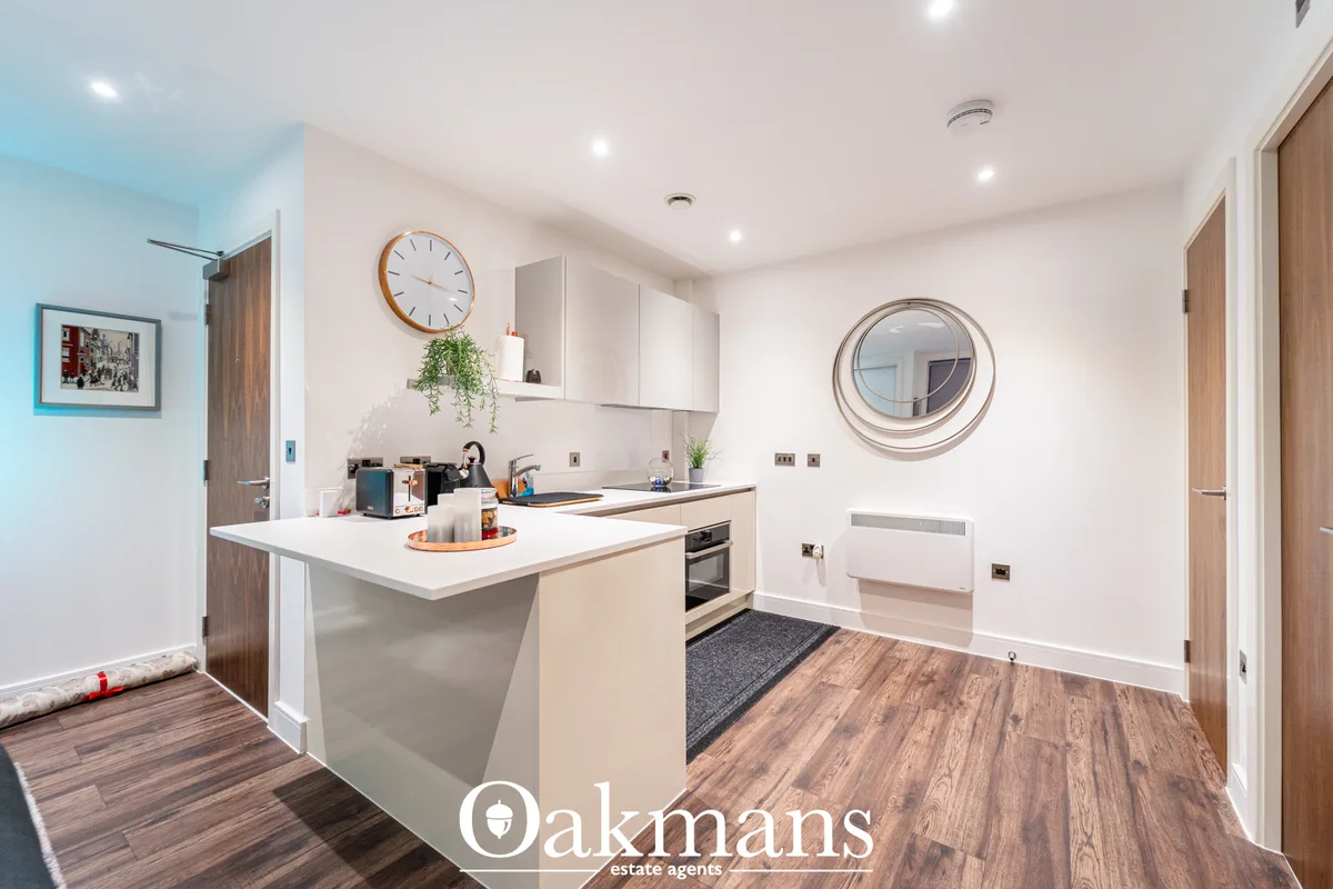 Modern kitchen with white cabinetry, beige island with white worktop, integrated appliances, wooden flooring, and circul