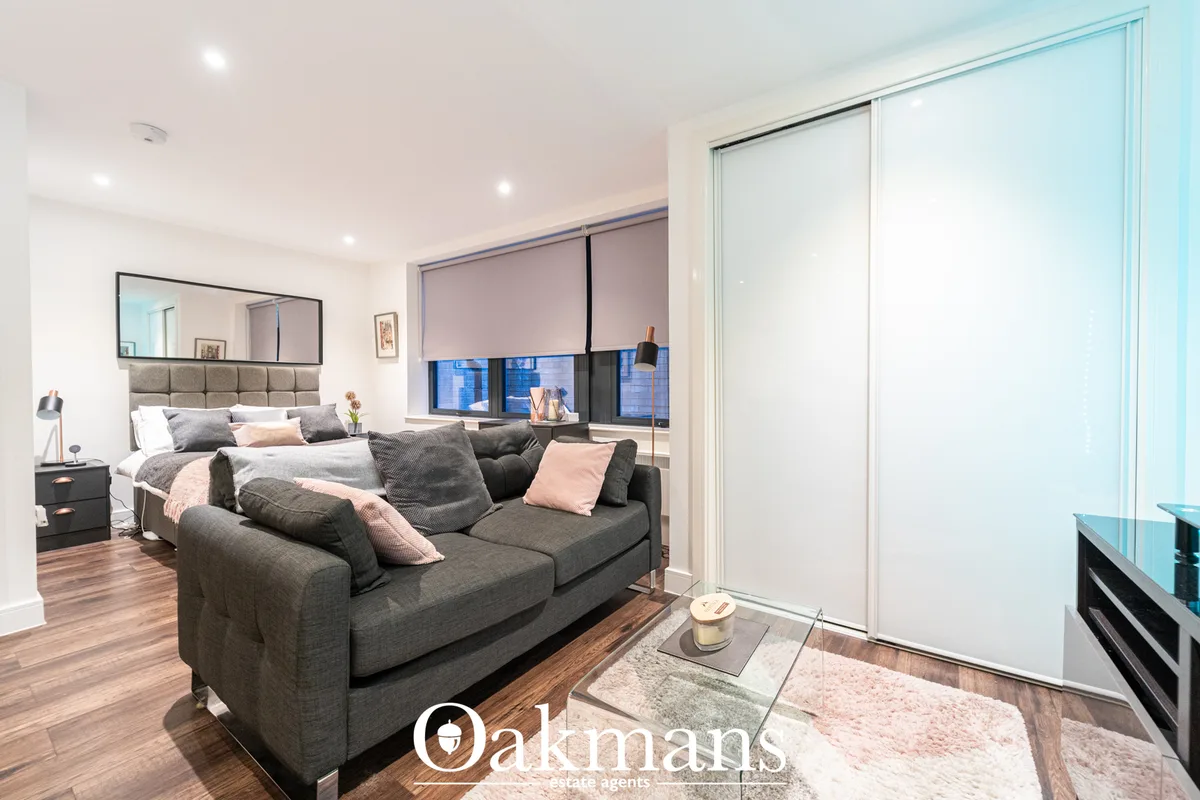Modern living room with charcoal sofa, pink accents, wooden flooring, large windows with city views, and open-plan acces