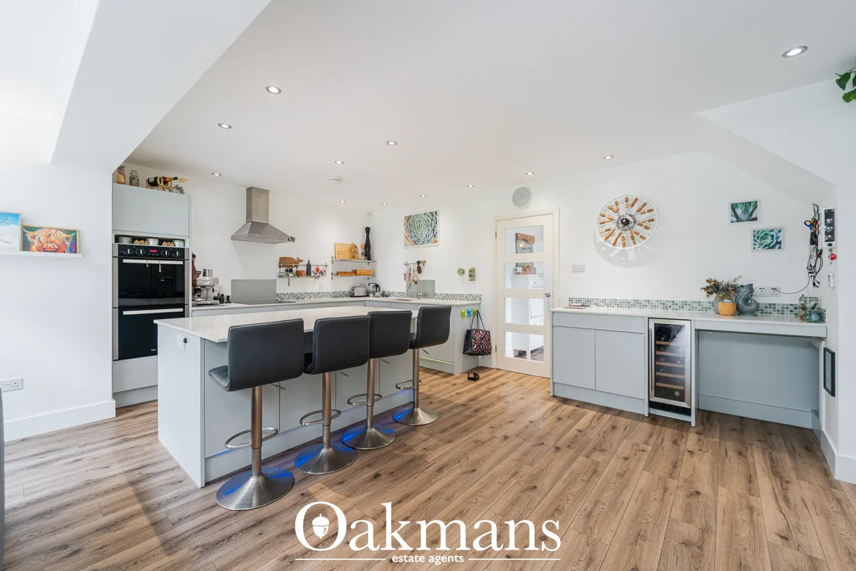 Modern open-plan kitchen with white cabinetry, stainless steel appliances, breakfast bar with black stools, and wood-eff