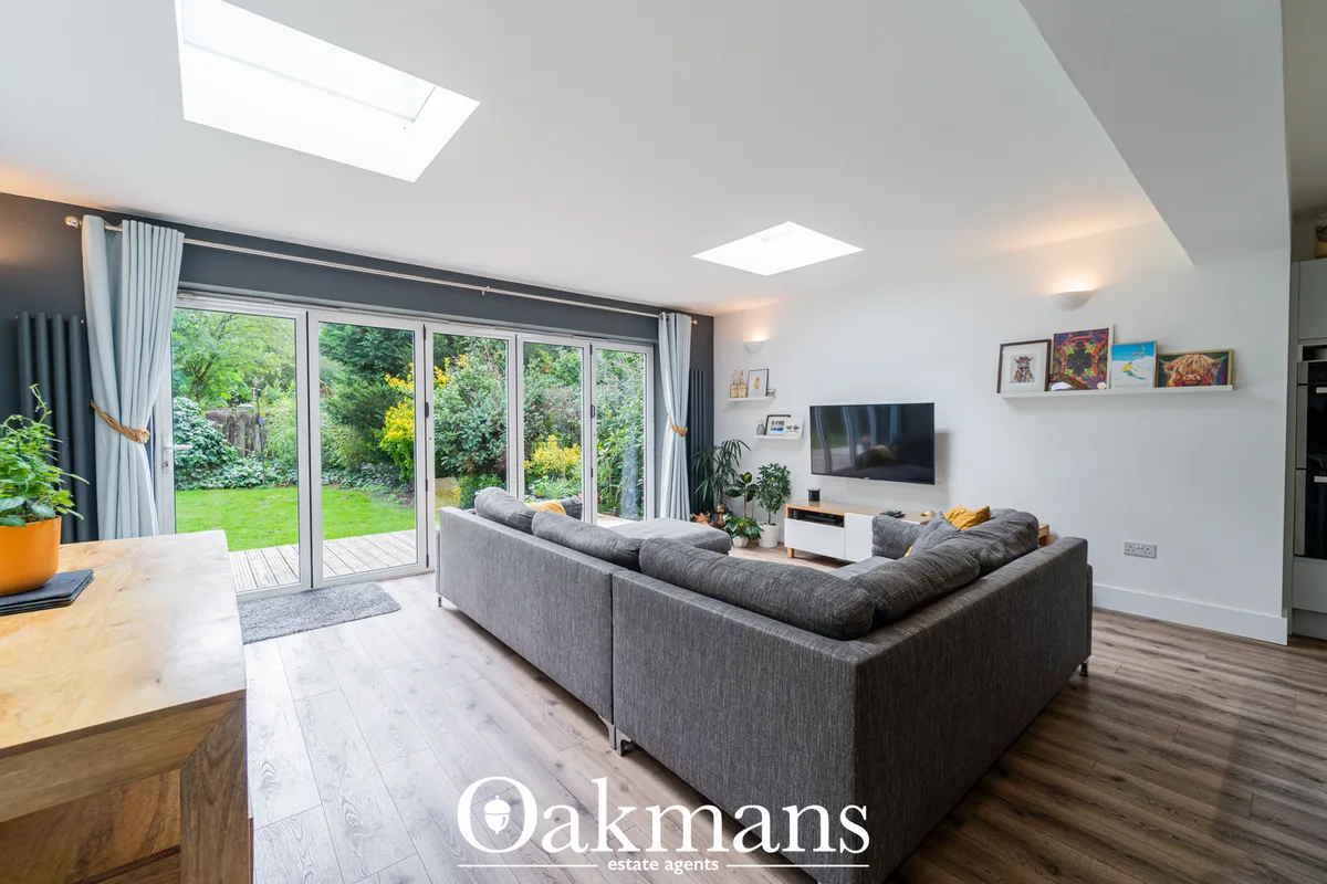 Modern open-plan living room with grey corner sofa, wall-mounted TV, skylights and bi-fold doors opening to garden