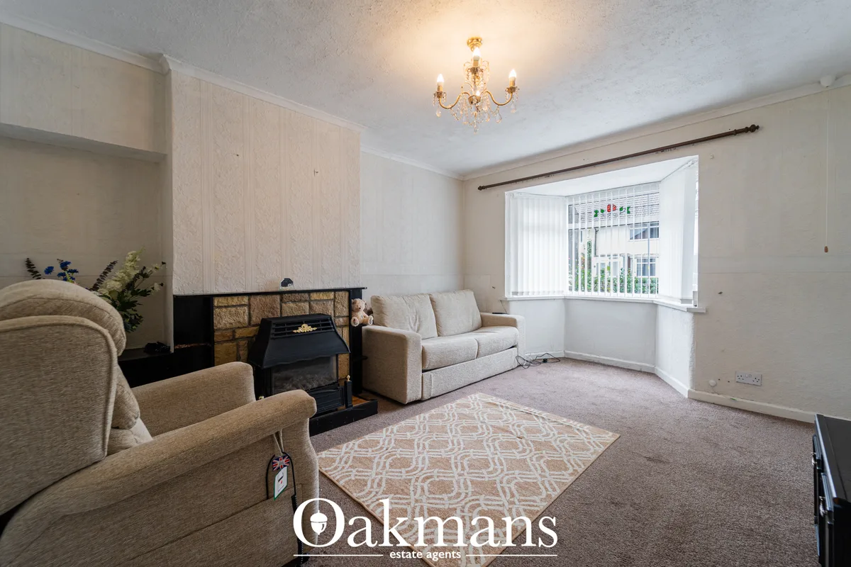 Spacious living room with beige fabric armchairs, sofa, fireplace with black surround, patterned rug, bay window with ve