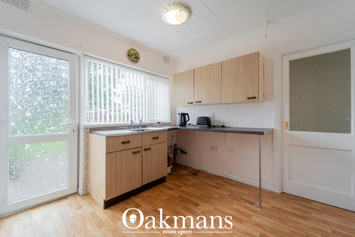 Modern kitchen with light wood cabinetry, grey worktops, white tile splashback, wooden flooring and garden access via pa