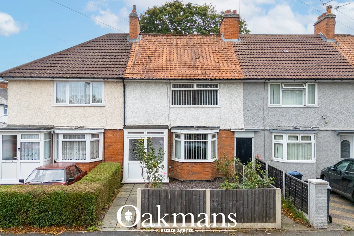 Terraced house with cream render, tiled roof, white bay windows, brick chimney stacks and small front garden with hedge