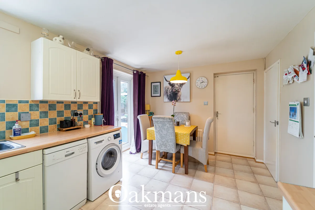 Open-plan kitchen and dining room with cream units, wooden worktops, teal and gold tile splashback, dining table and yel