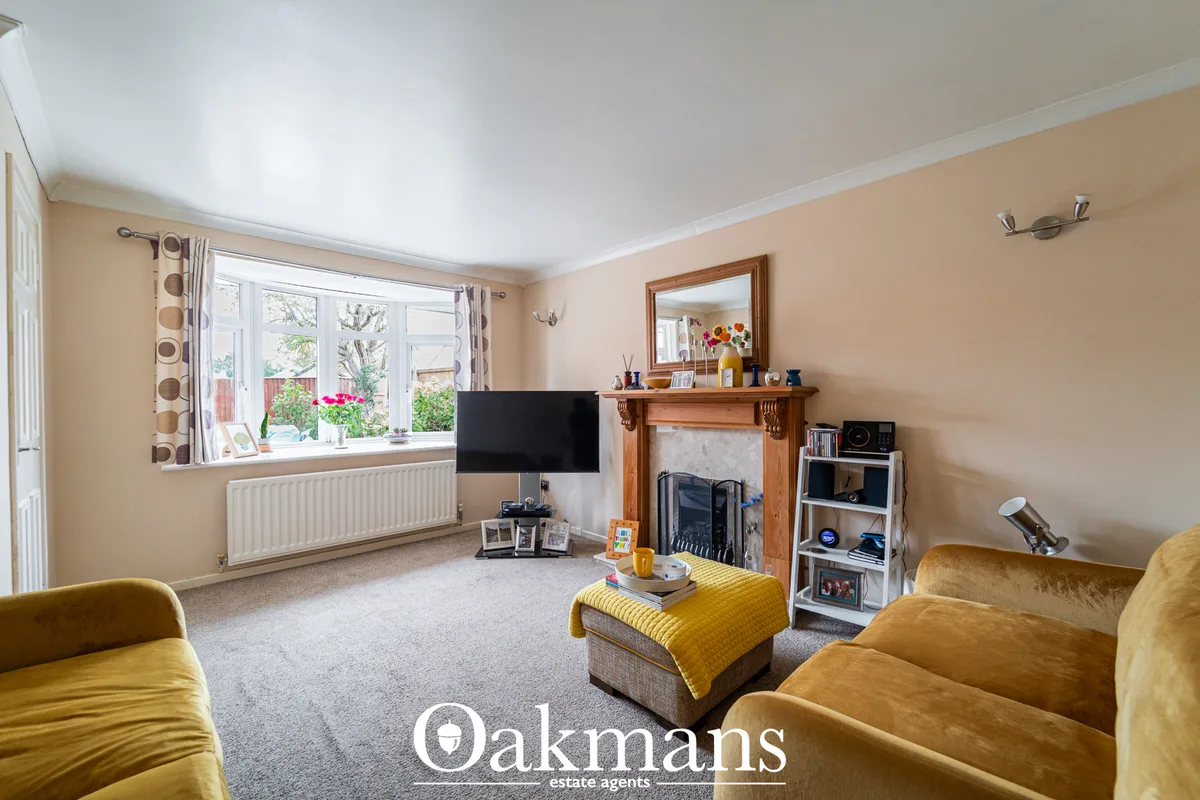 Spacious living room with peach walls, large bay window, wooden fireplace with mirror, yellow armchairs, TV on stand, sh