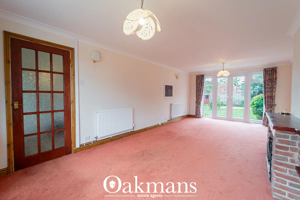 Spacious living room with pink carpet, cream walls, French doors to garden, patterned curtains, radiator, cream ceiling 