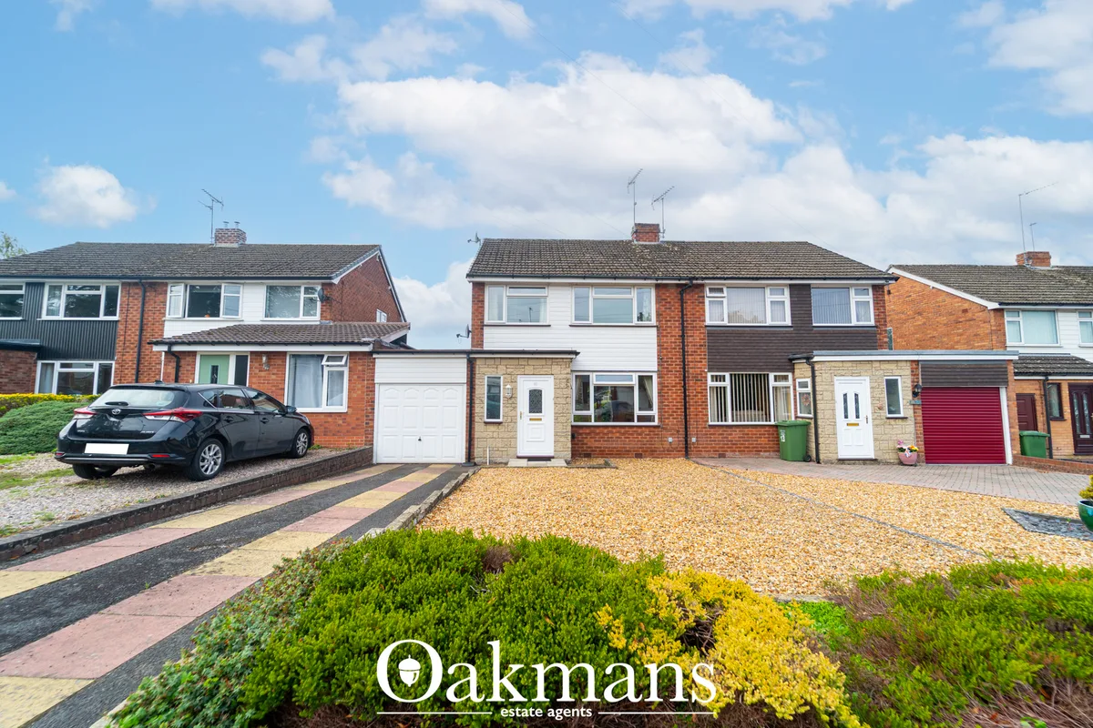 Row of brick-built semi-detached houses with driveways, parked car, gravel forecourts and landscaped gardens under blue 