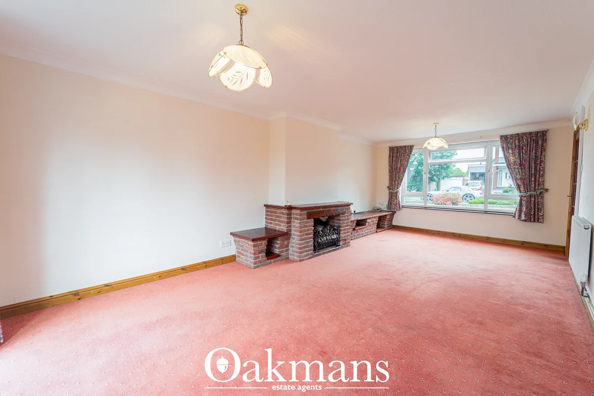 Spacious living room with brick fireplace, pink carpet, large window with patterned curtains, wooden trim, and pendant l