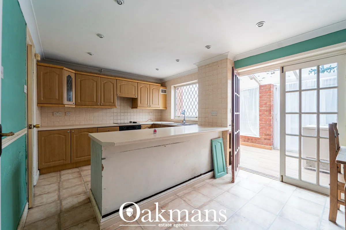 Kitchen with wooden cabinets, cream tile splashback, central island, French doors to garden, recessed ceiling lights and
