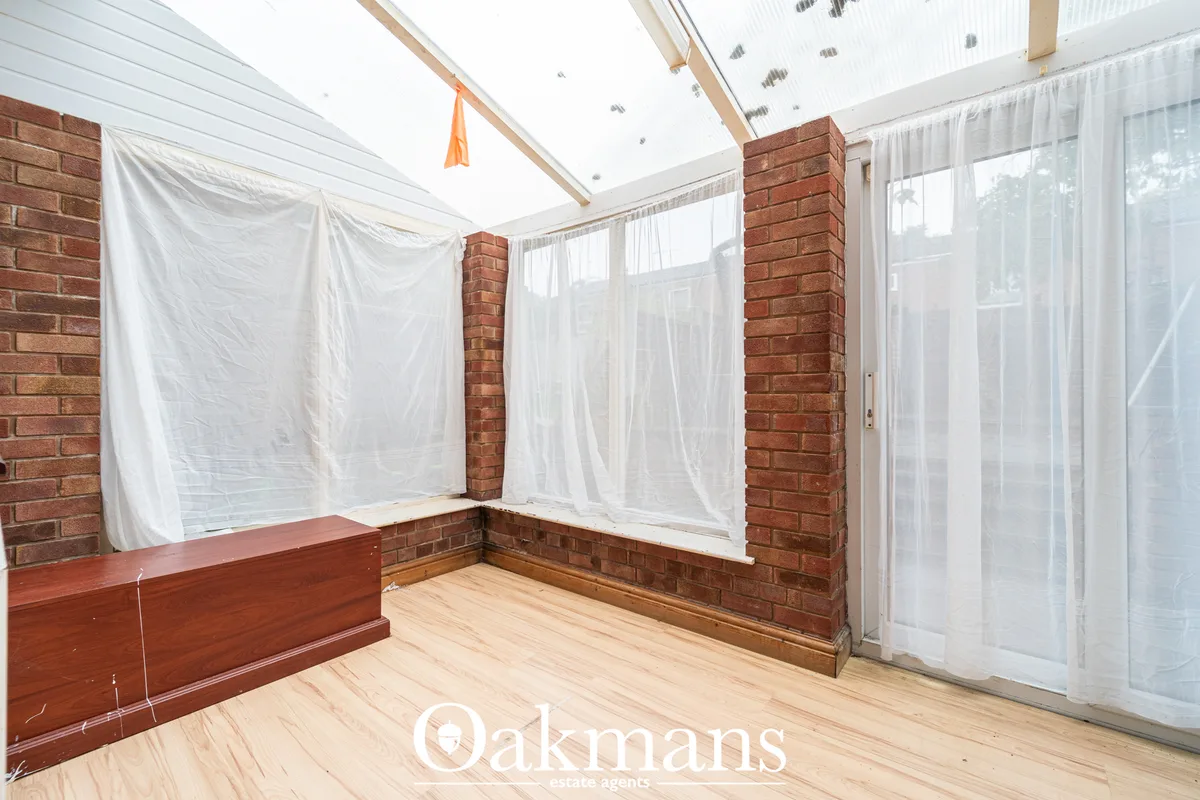 Bright conservatory with exposed red brick pillars, wooden flooring, white sheer curtains, glass roof panels and skyligh