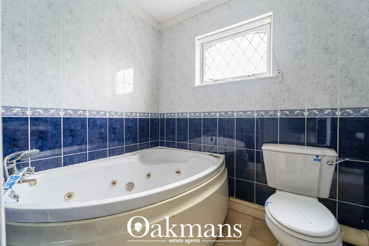 Modern bathroom with corner Jacuzzi tub, white suite, blue and white tilework, window with leaded glass