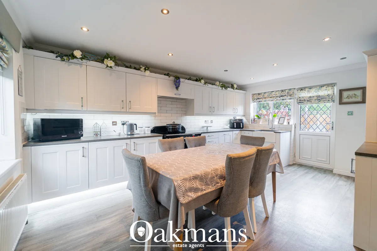 Modern white fitted kitchen with dining area, round table, four upholstered chairs, grey worktops, subway tile splashbac