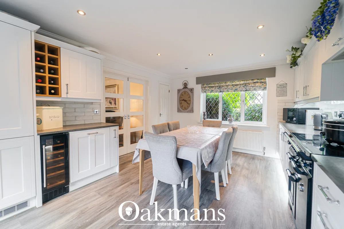 Modern open-plan kitchen-diner with white cabinetry, dining table with grey upholstered chairs, and bifold doors to gard