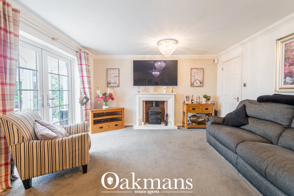 Spacious living room with cream walls, grey sofa, striped armchair, fireplace with stove, TV above mantelpiece, crystal 