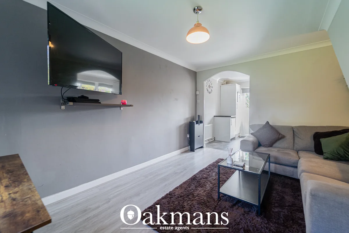 Modern living room with grey sofa, glass coffee table, wall-mounted TV, wooden flooring and access to kitchen area