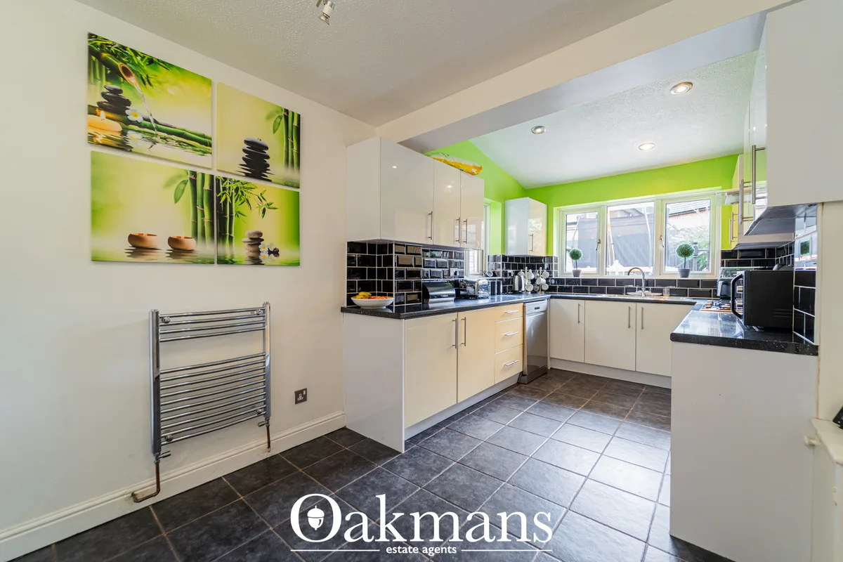 Modern fitted kitchen with cream units, black granite worktops, black subway tiled backsplash, stainless steel appliance