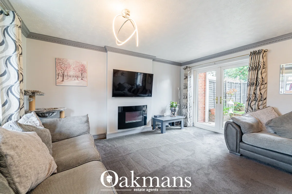 Spacious living room with grey upholstered seating, wall-mounted TV, electric fireplace, neon wall light, and French doo
