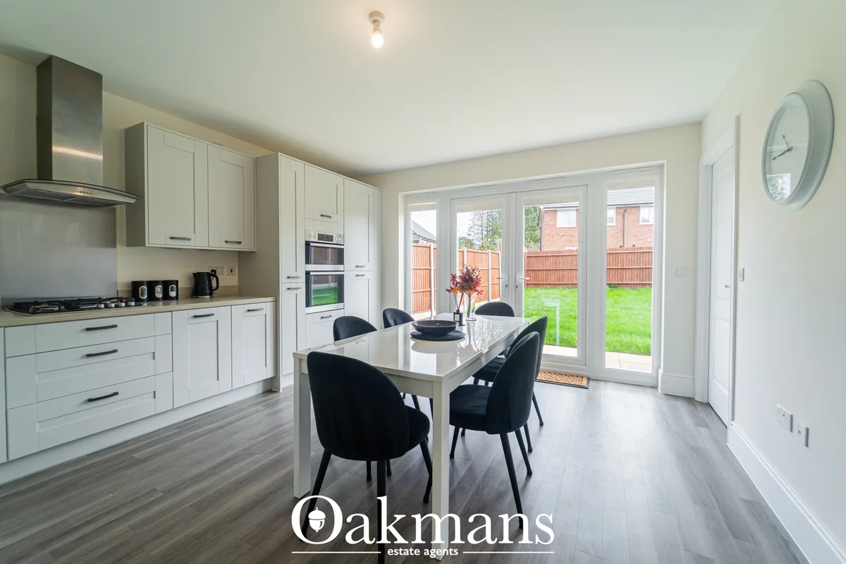 Modern white fitted kitchen with integrated appliances, breakfast bar, dining table with black chairs, and bi-fold doors