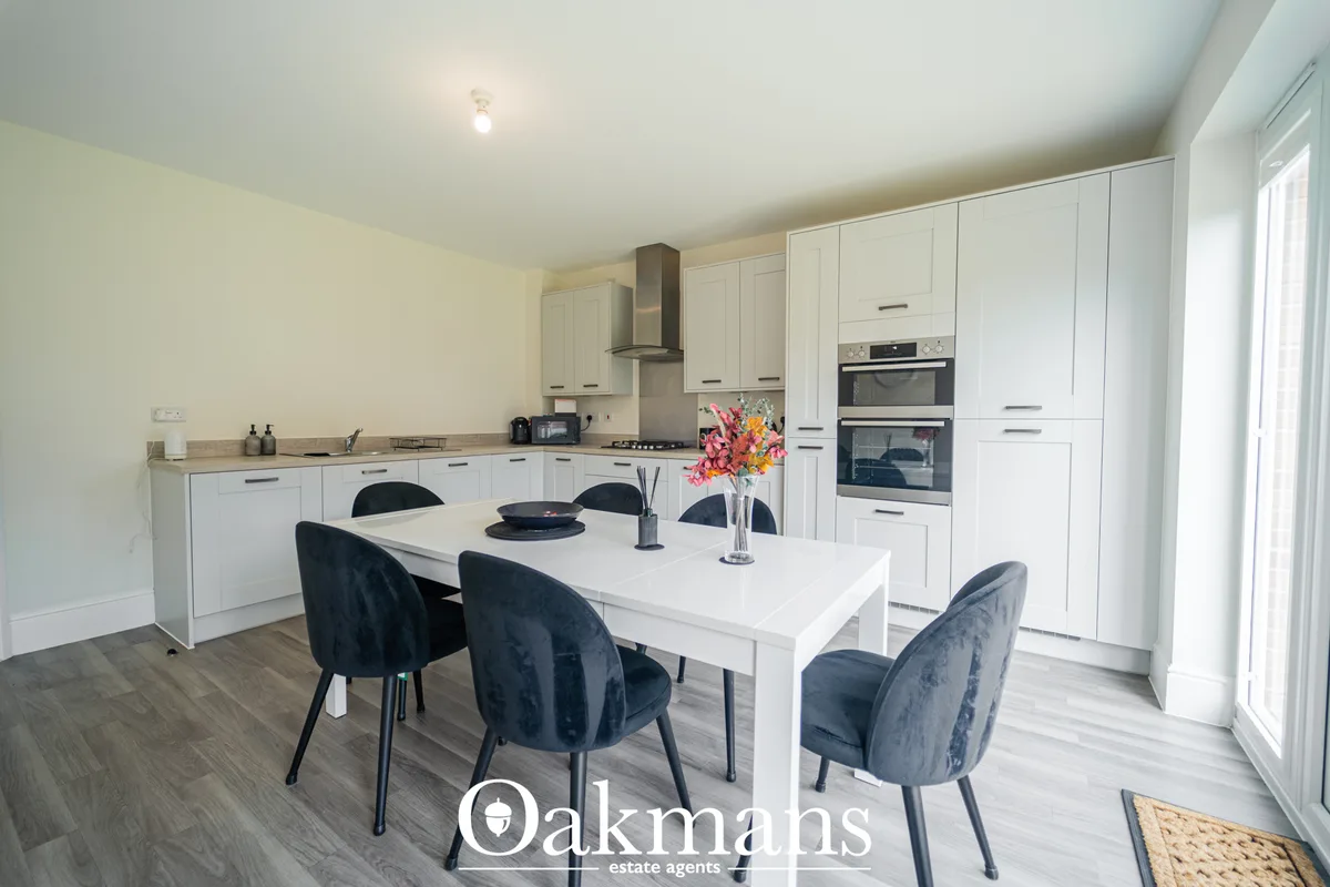 Modern white fitted kitchen with island, dining table, black chairs, dual ovens, gas hob and stainless steel hood