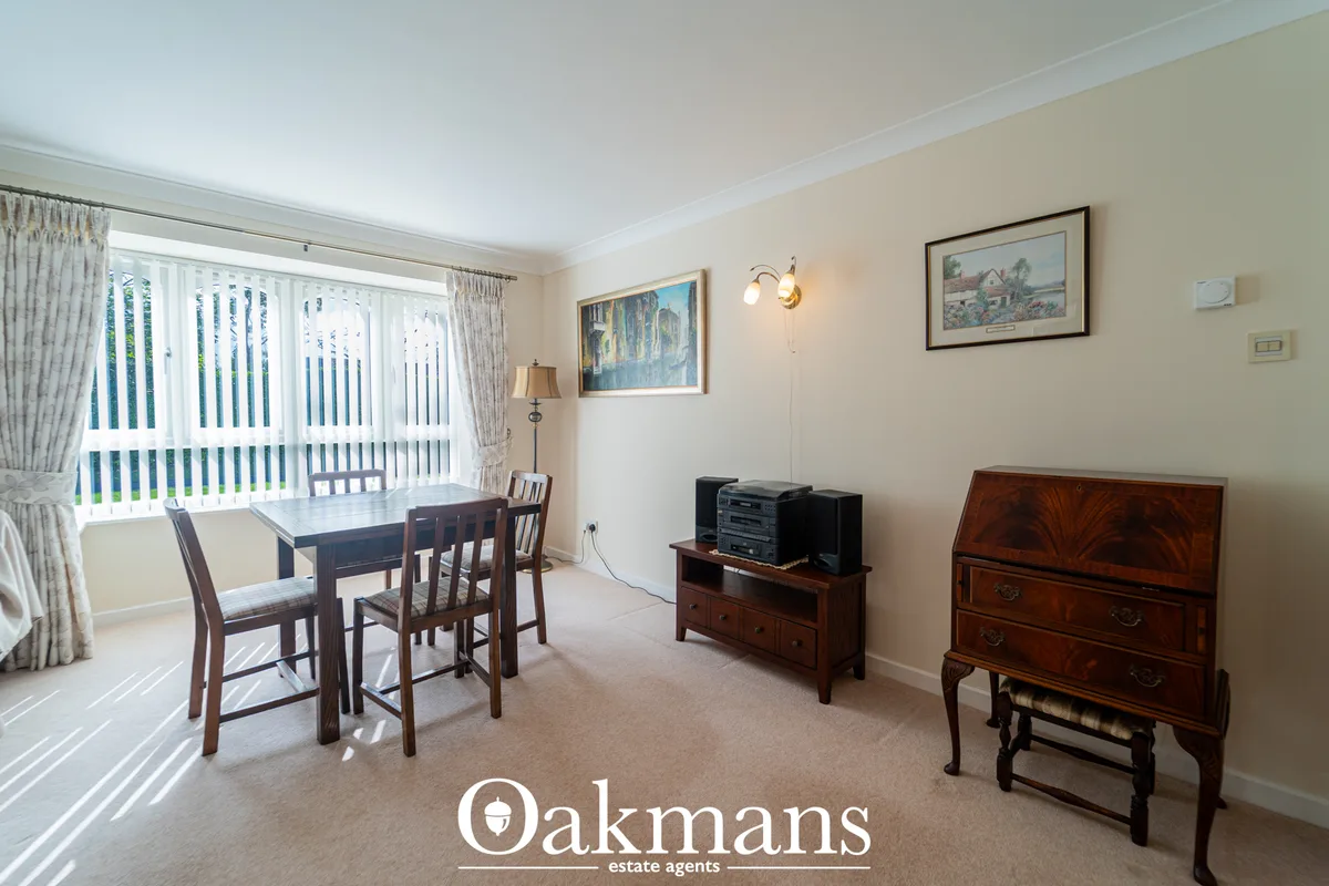 Bright dining room with dark wood table and chairs, cream carpet, large window with vertical blinds, framed artwork and 