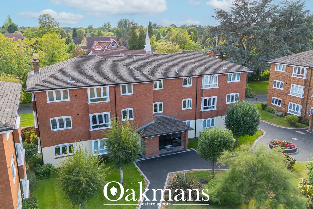 Aerial view of brick residential building with slate roof, driveway entrance, manicured grounds and surrounding trees