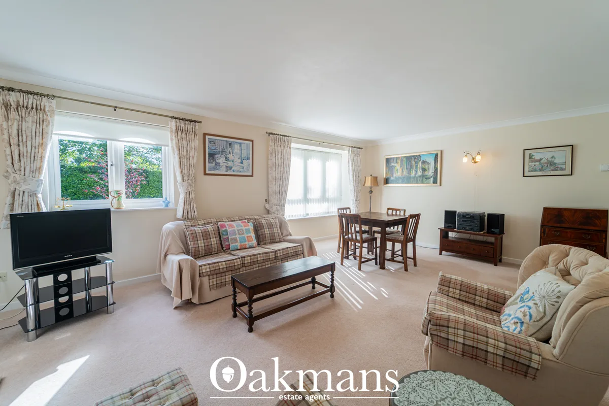 Spacious living room with cream carpet, plaid sofa, armchair, wooden furniture, TV, dining table, multiple windows with 