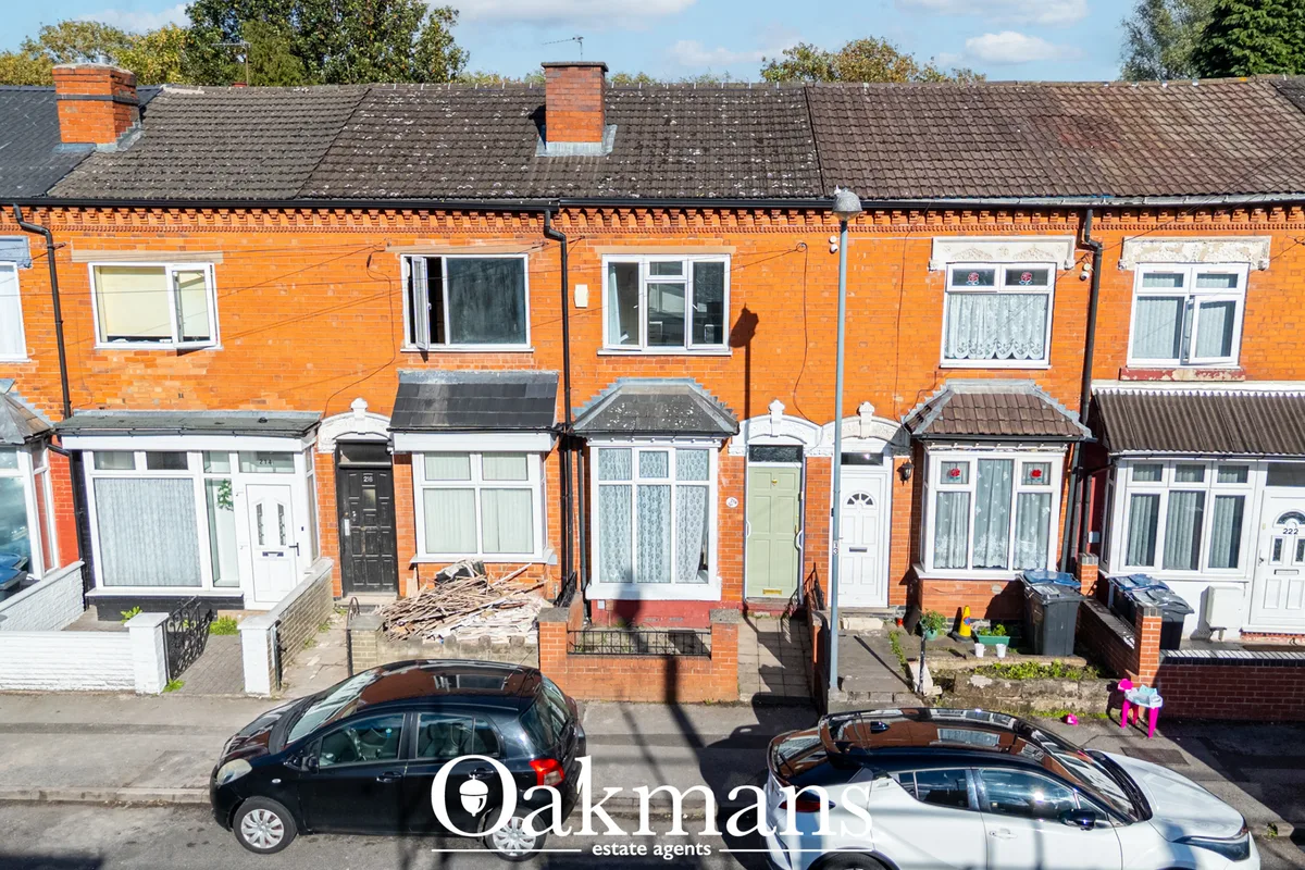 Aerial view of a row of orange-brick terraced houses with slate roofs, white-framed doors and windows, parked cars on st