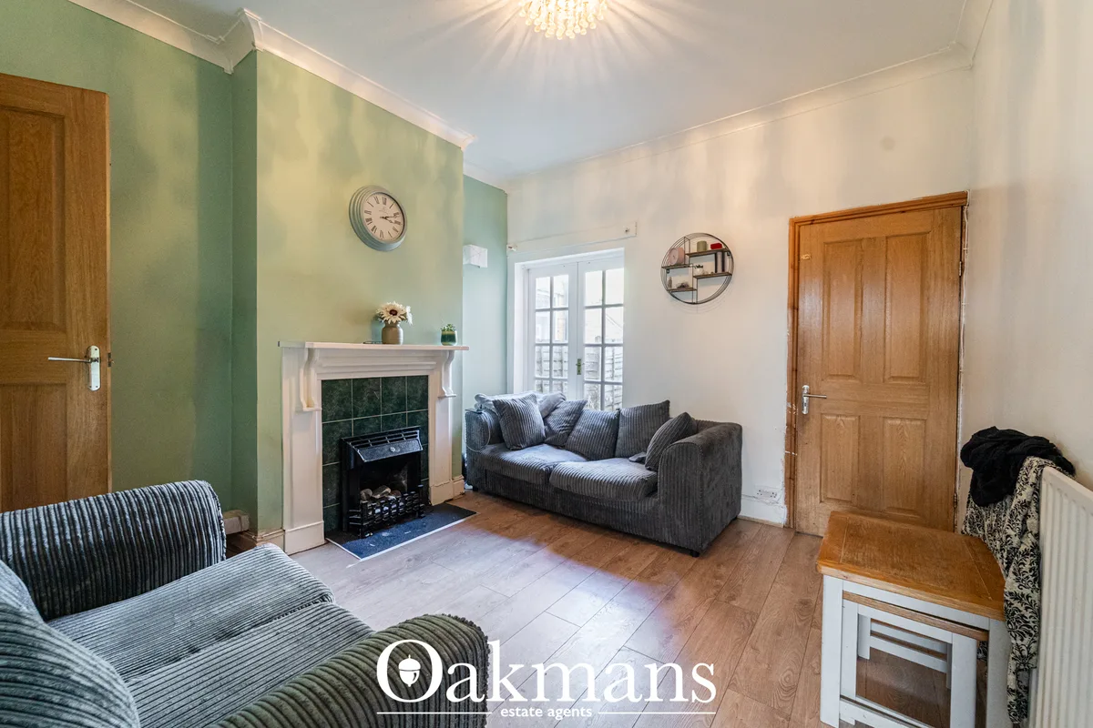 Spacious living room with green accent wall, fireplace with black surround, grey upholstered sofa with scatter cushions,
