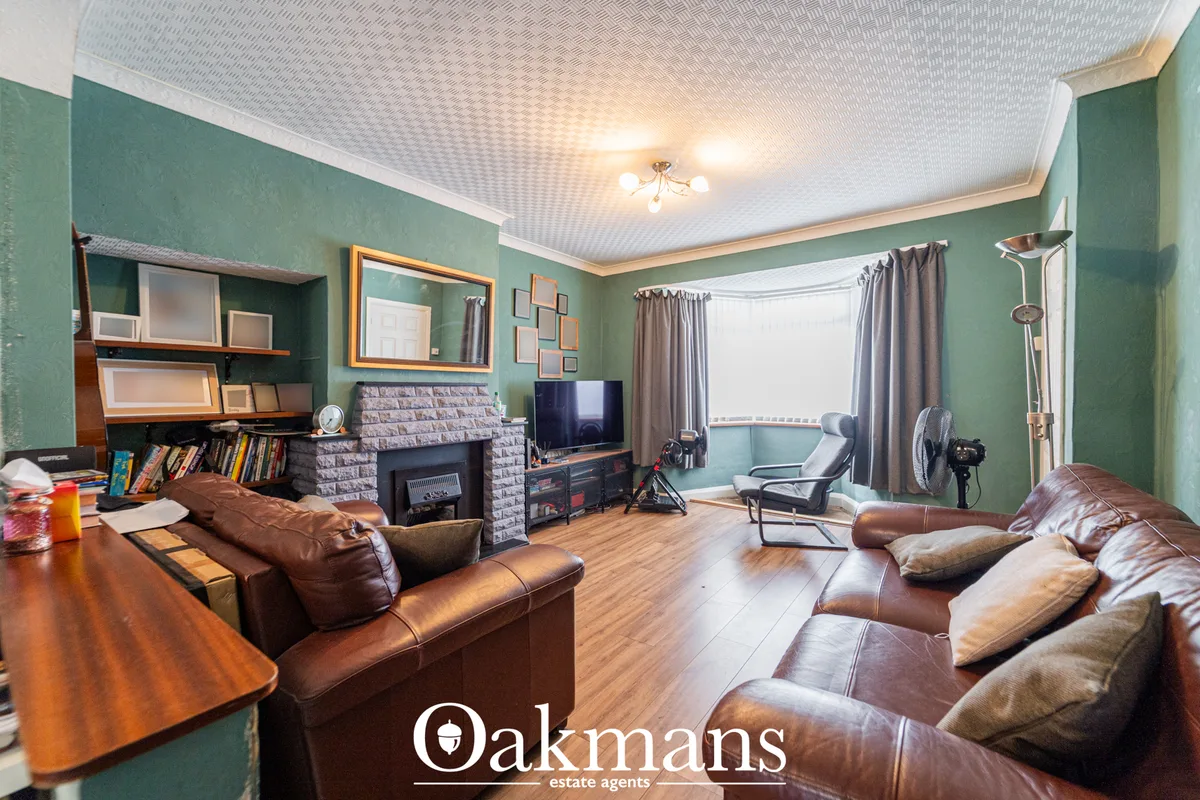 Spacious living room with green walls, brown leather sofas, fireplace with brick surround, wooden flooring, bay window w