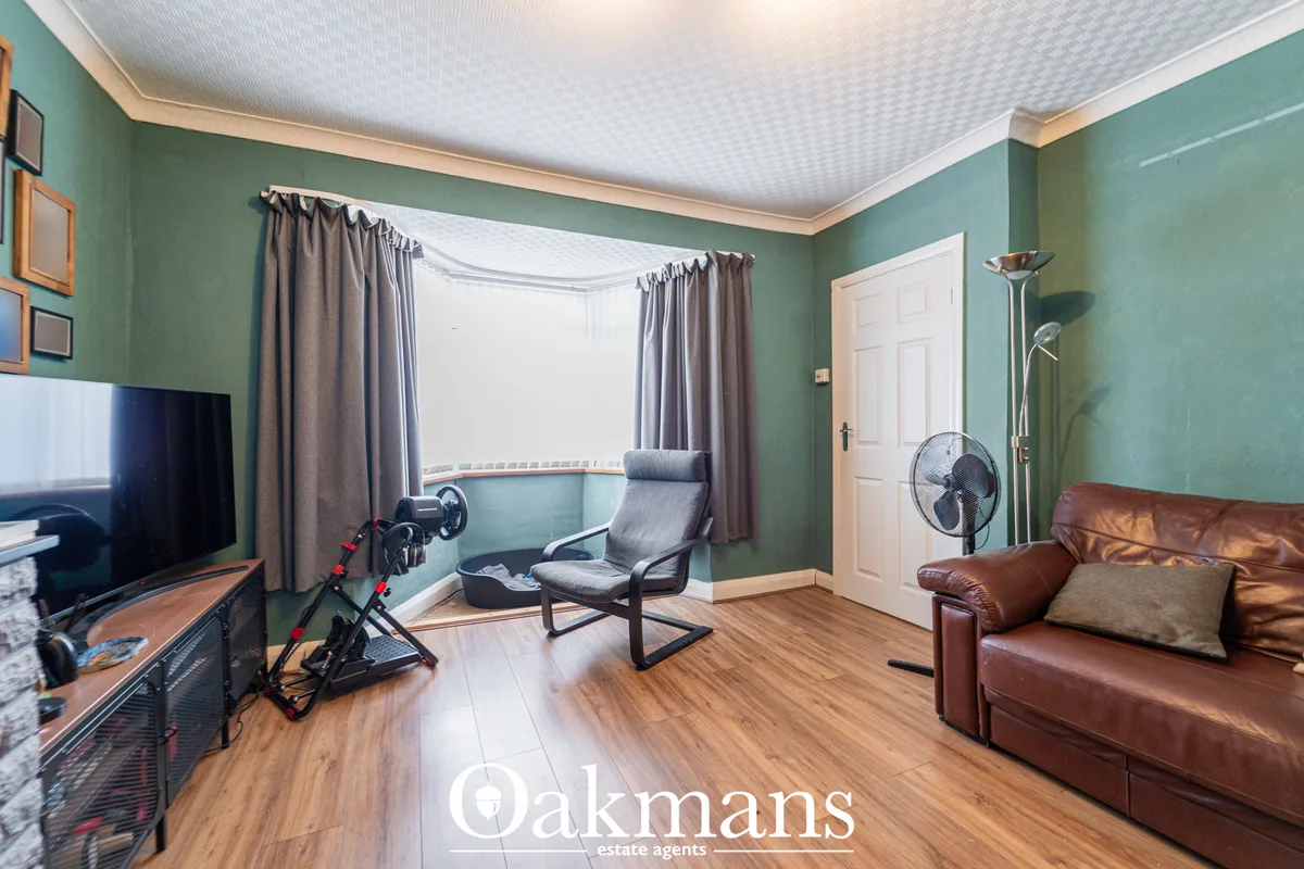 Spacious living room with mint-green walls, bay window with grey curtains, brown leather sofa, gaming chair, TV, wooden 