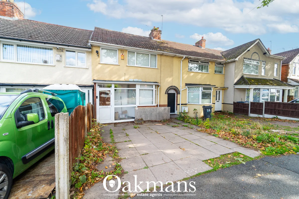 Terraced house with yellow render, white-framed windows, black front door, driveway with green van parked, autumn leaves