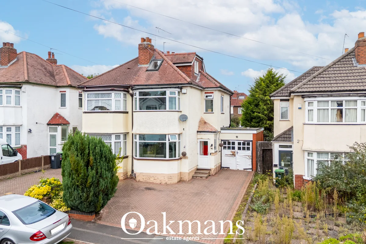 Semi-detached cream and white brick house with tiled roof, driveway, and manicured front garden in residential suburban 
