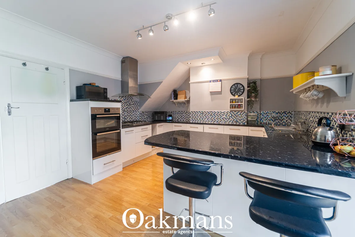 Modern fitted kitchen with white units, black granite worktops, breakfast bar seating, mosaic tile splashback, integrate