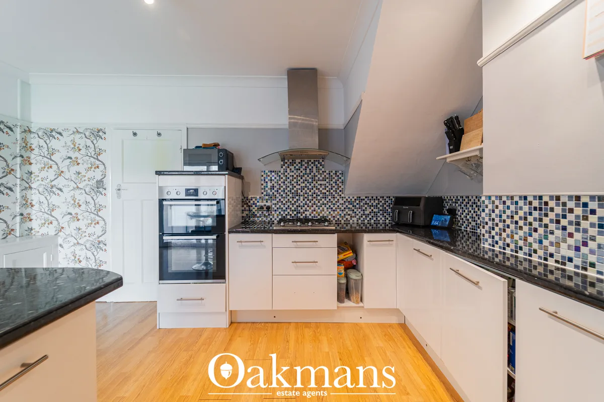 Modern fitted kitchen with cream units, black worktops, mosaic tile splashback, built-in oven, wood flooring and skyligh
