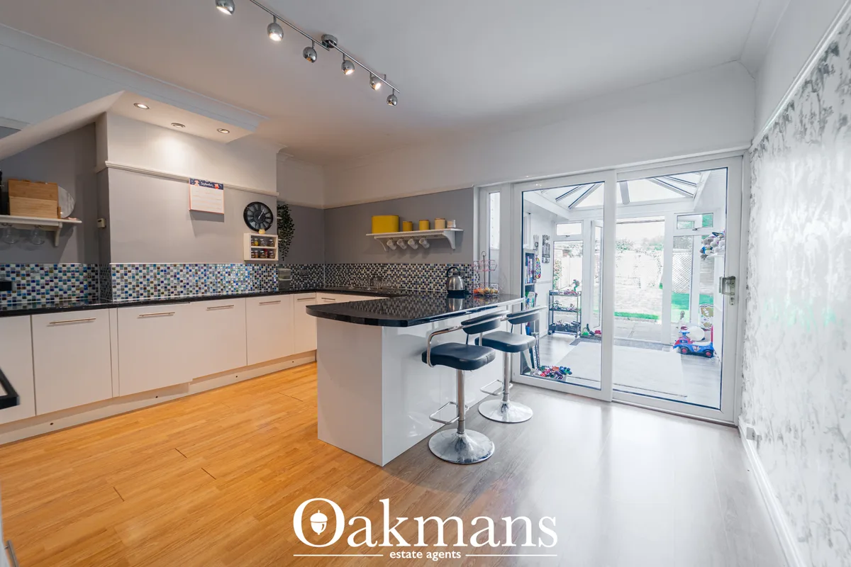 Modern open-plan kitchen with white fitted units, blue mosaic tile splashback, black worktops, breakfast bar with stools
