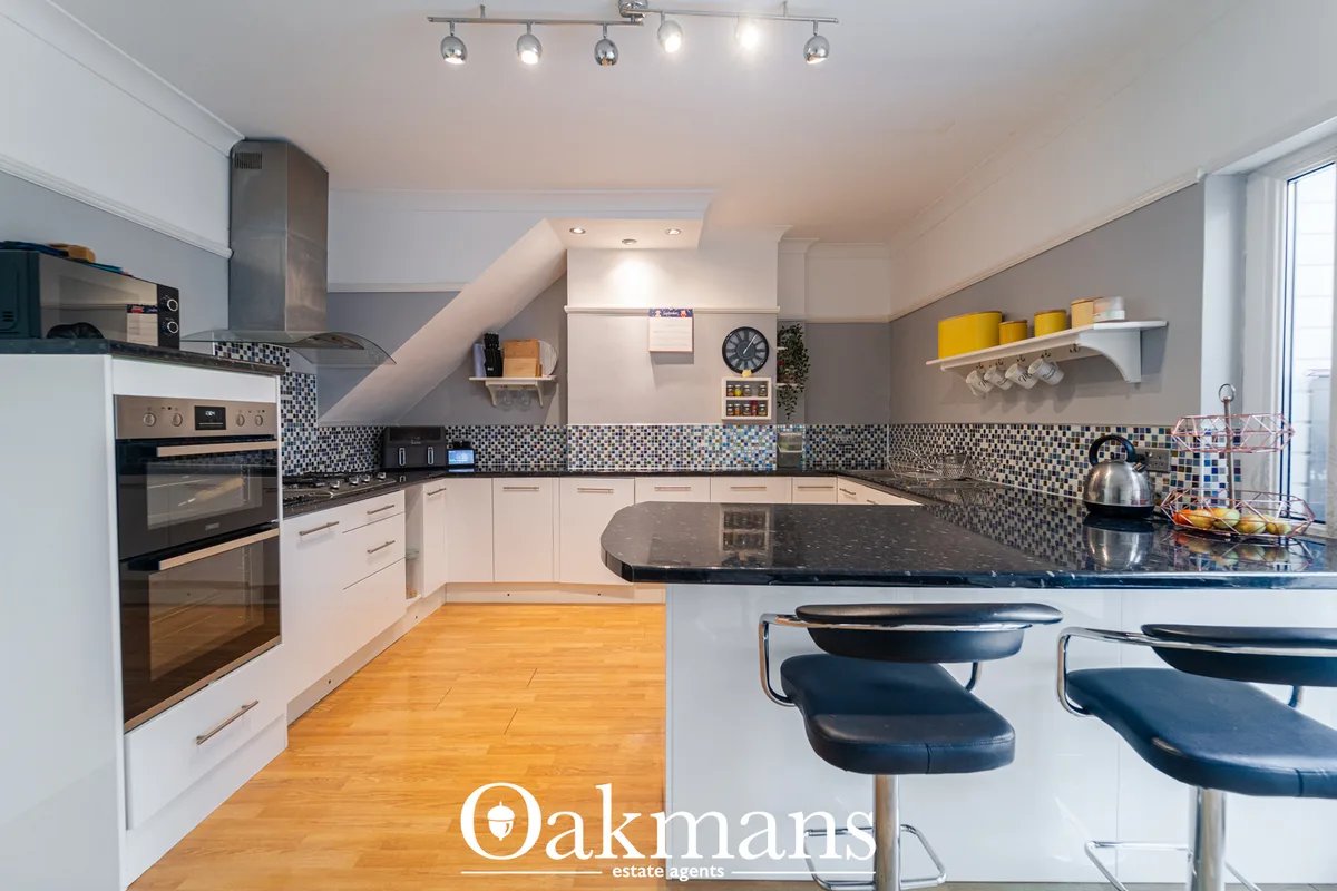 Modern fitted kitchen with white cabinetry, dark granite worktops, geometric mosaic splashback, stainless steel applianc